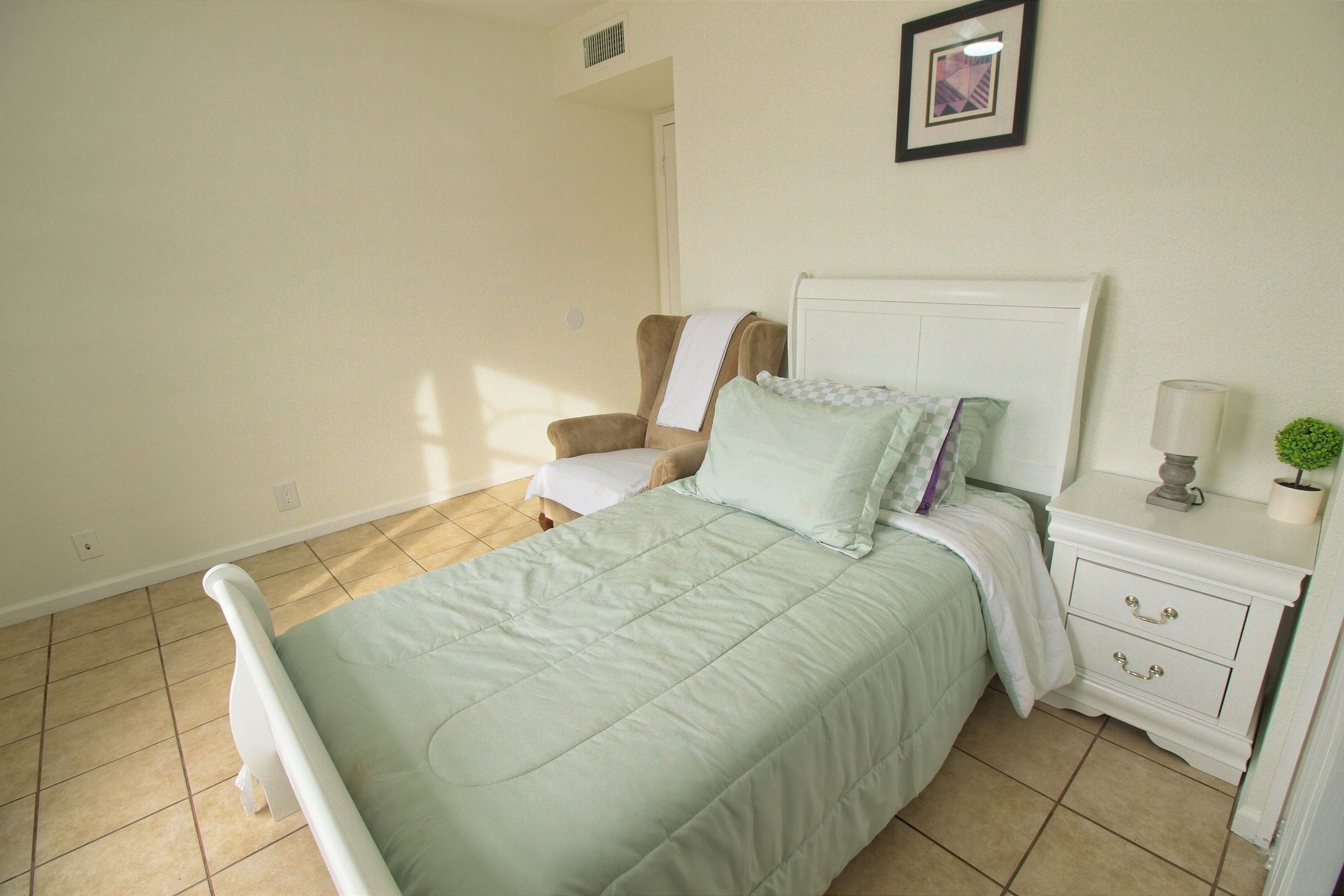 A private bedroom with a white sleigh bed, a wingback chair and a nightstand