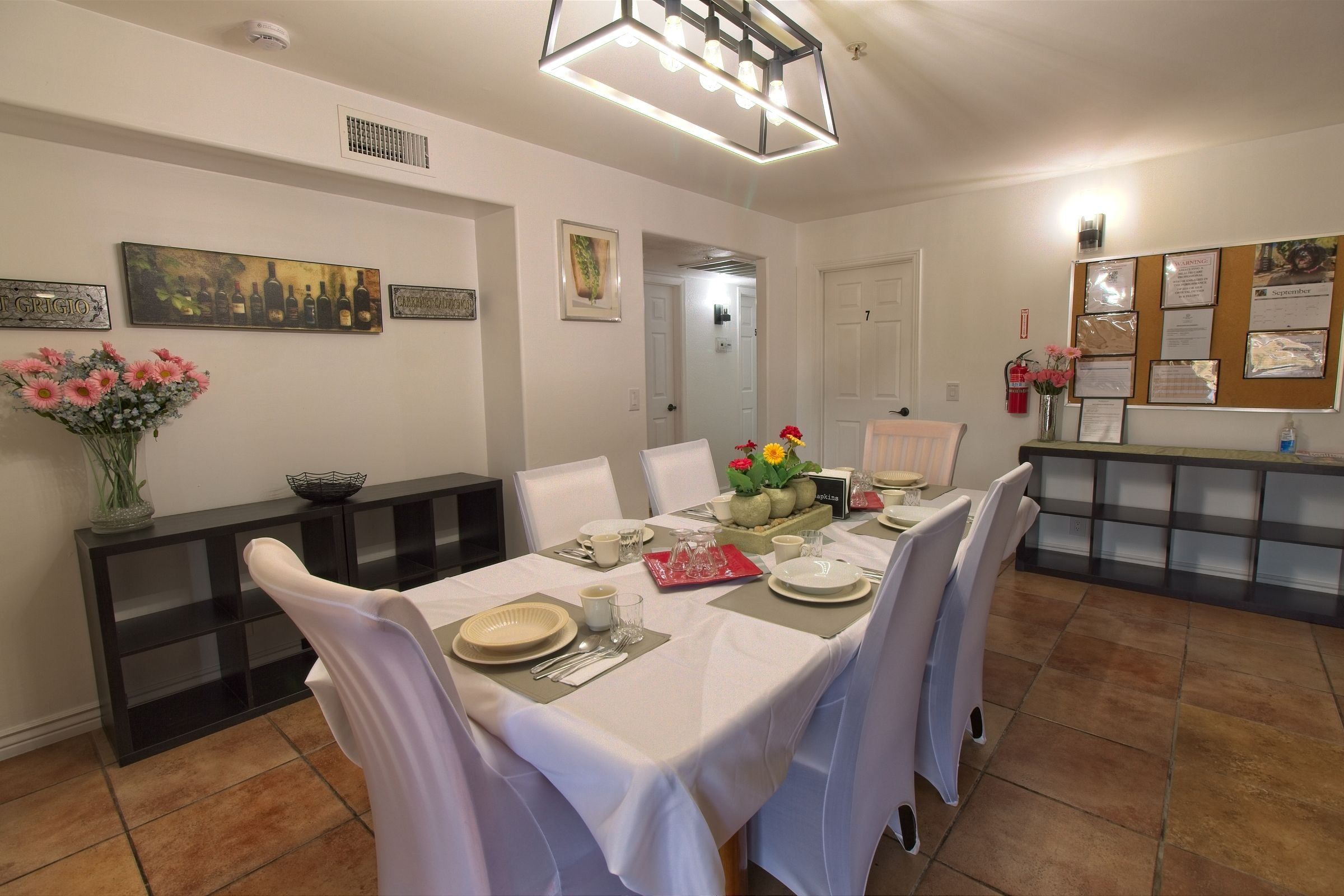 The dining room: a table with a white cloth and fresh flowers, chairs in white covers, and shelving along the walls