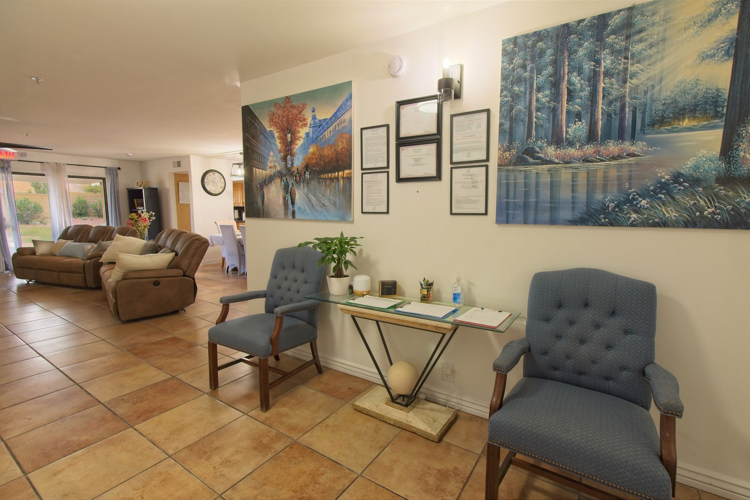 The sitting area inside the front door, with two blue armchairs, a glass console table and paintings on the wall