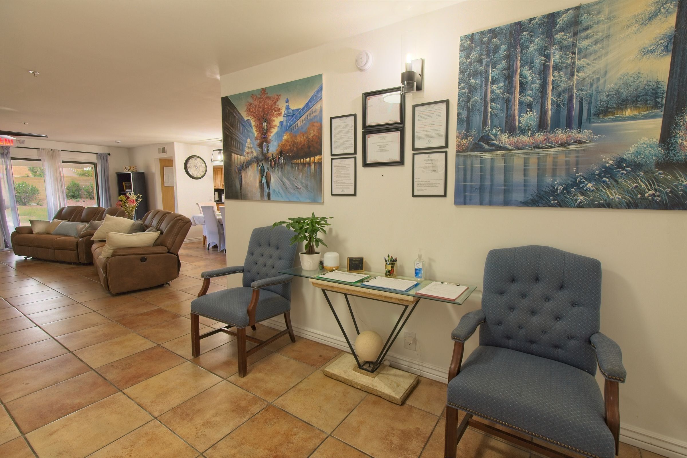 The sitting area inside the front door, with two blue armchairs, a glass console table and paintings on the wall
