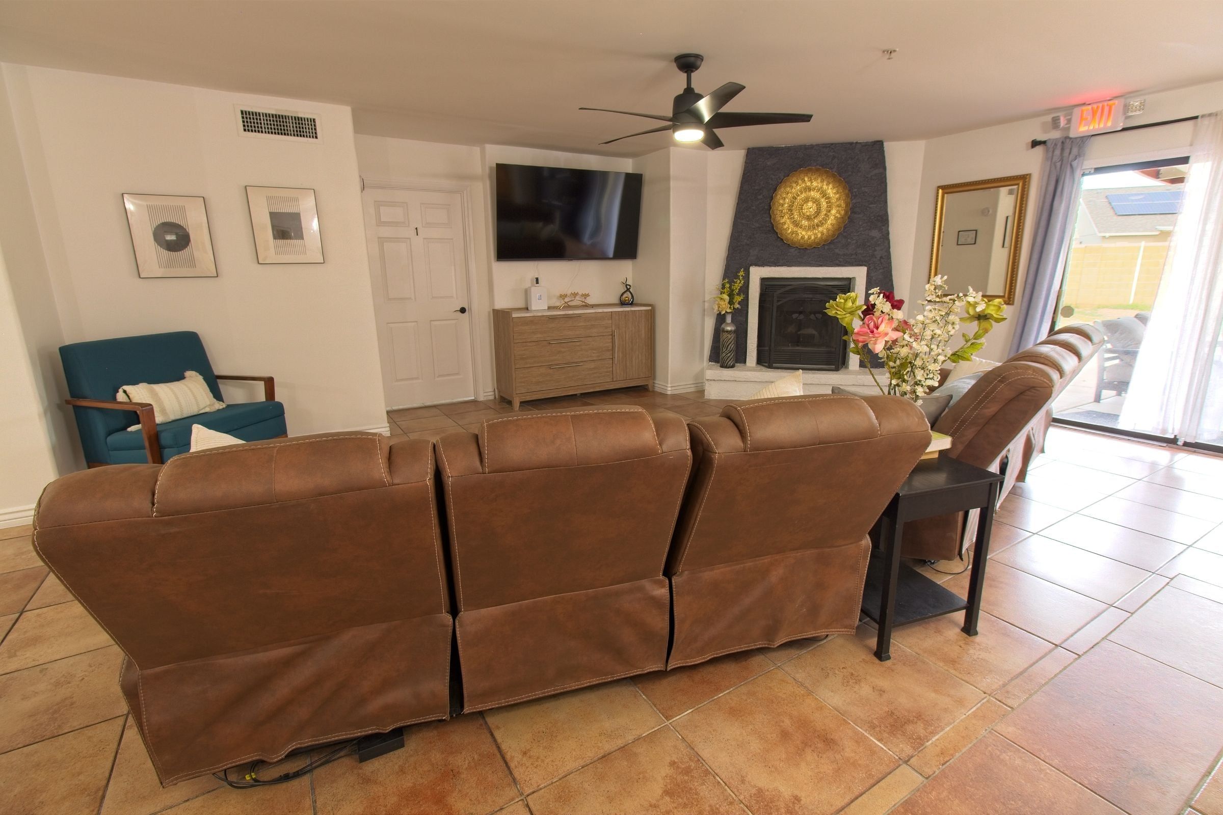 The living room, with a fireplace, a wall-mounted television, recliner sofas and glass doors onto the back patio