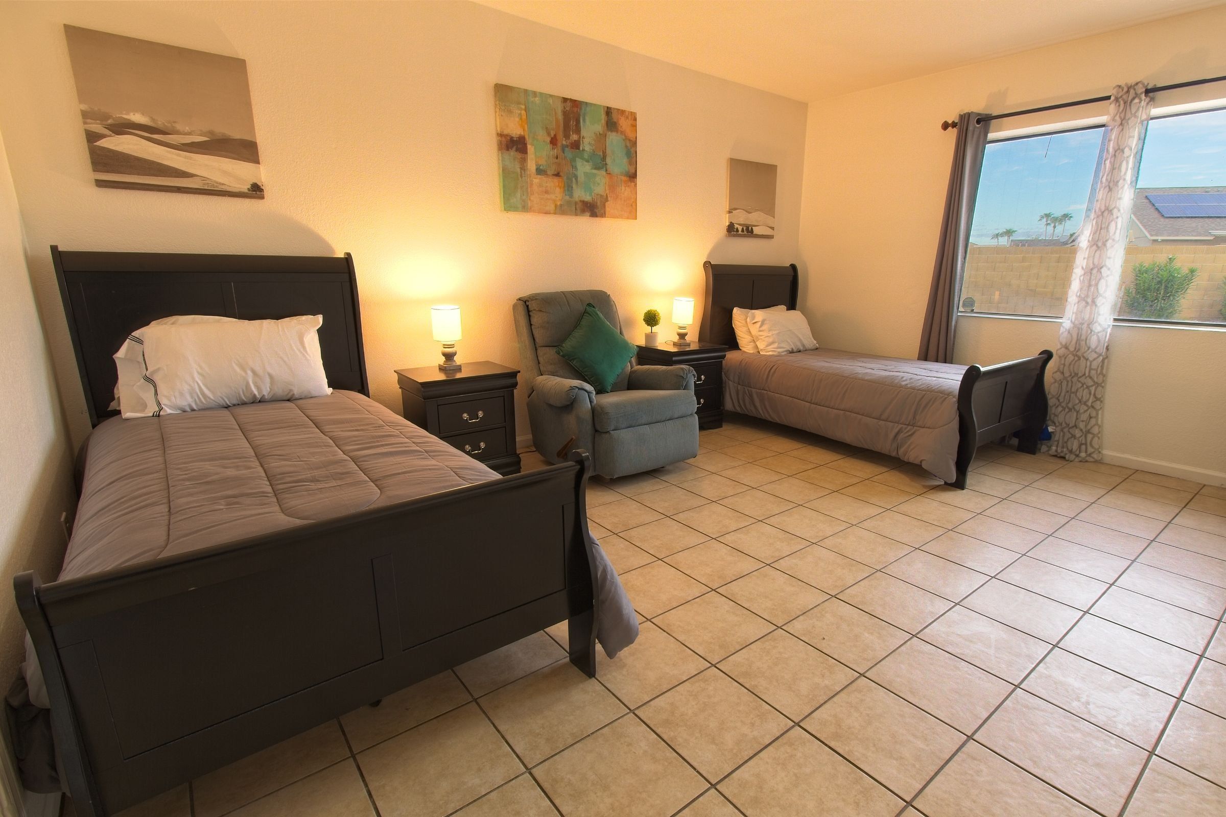 A shared bedroom with two dark wood beds, a recliner and a large window