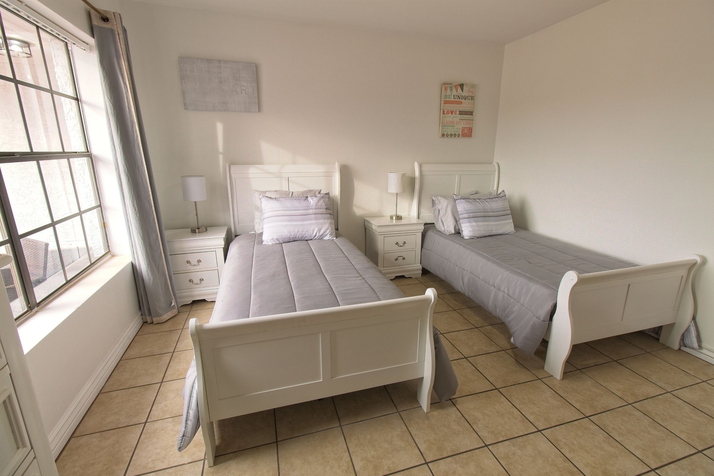 A shared bedroom with two white beds by a large window